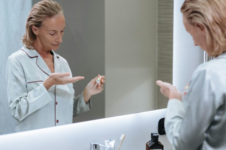 Femme appliquant un soin visage devant un miroir de salle de bain lumineuse