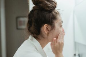Femme appliquant un sérum sur son visage devant un miroir, routine skincare matinale